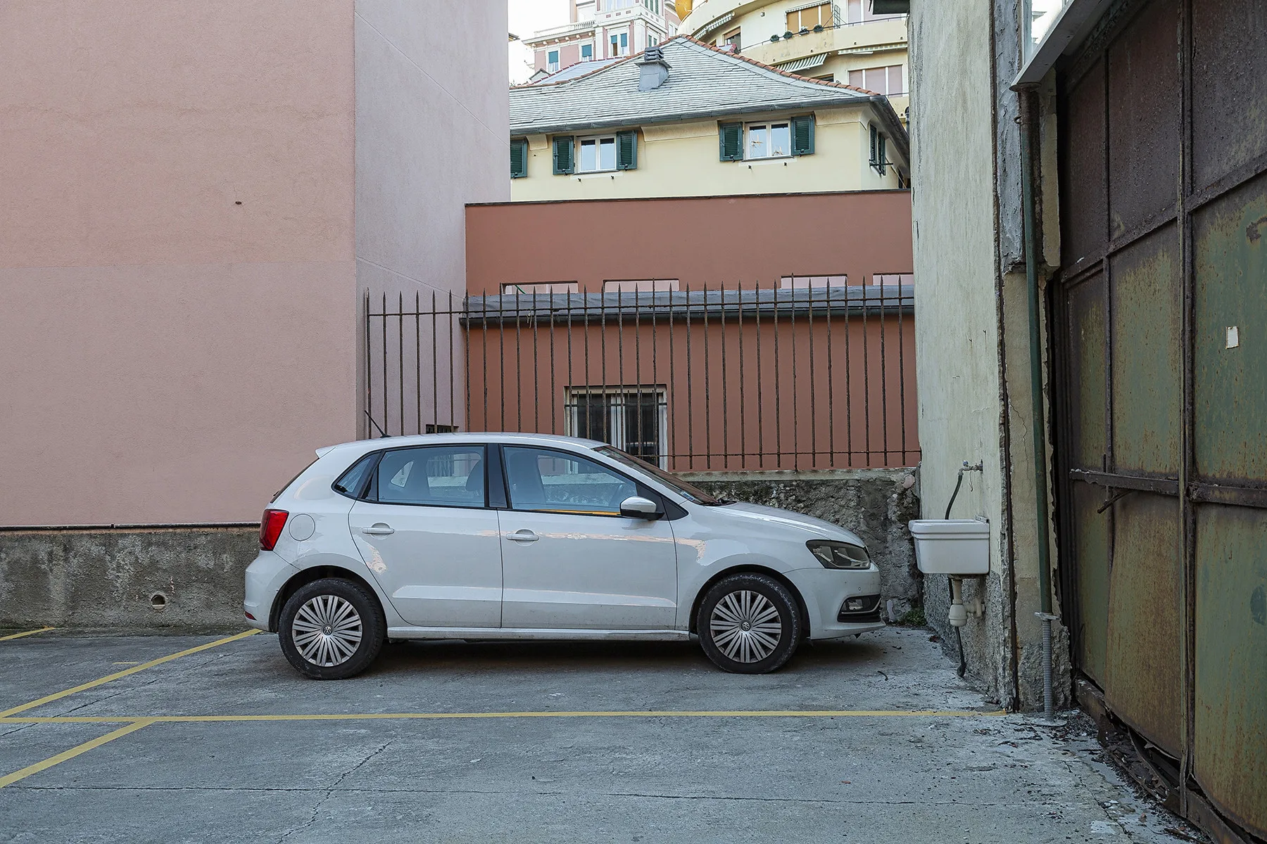 A silver car is parked in a paved courtyard beside a metal gate.
