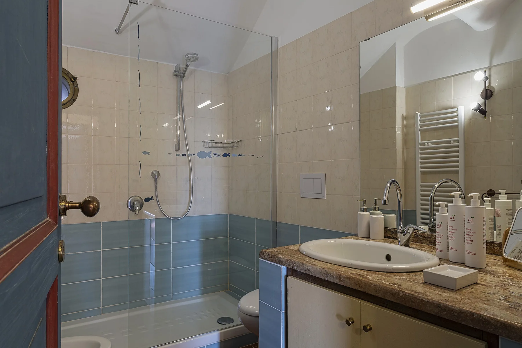 A tiled bathroom with a glass shower and a sink beneath a large mirror.