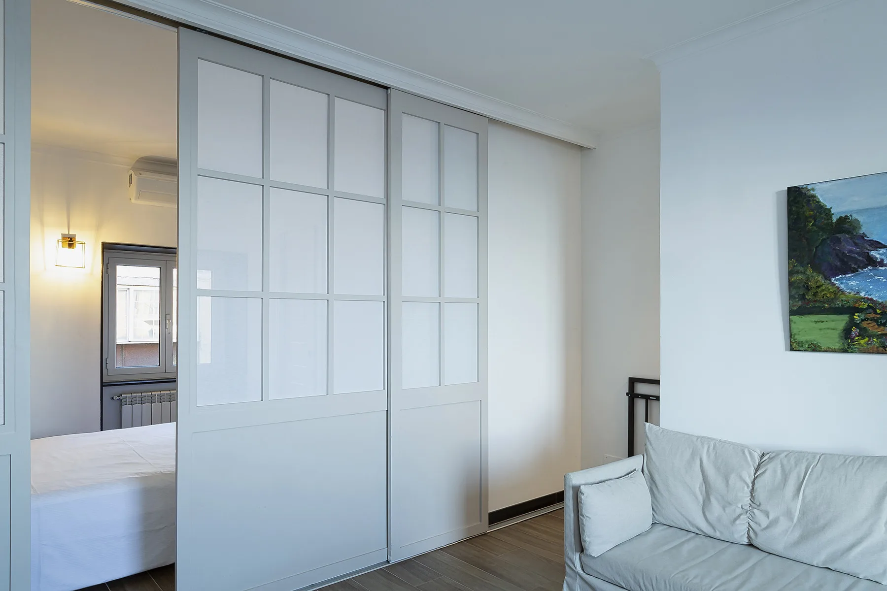 A bright bedroom with a large white sliding partition and a bed.