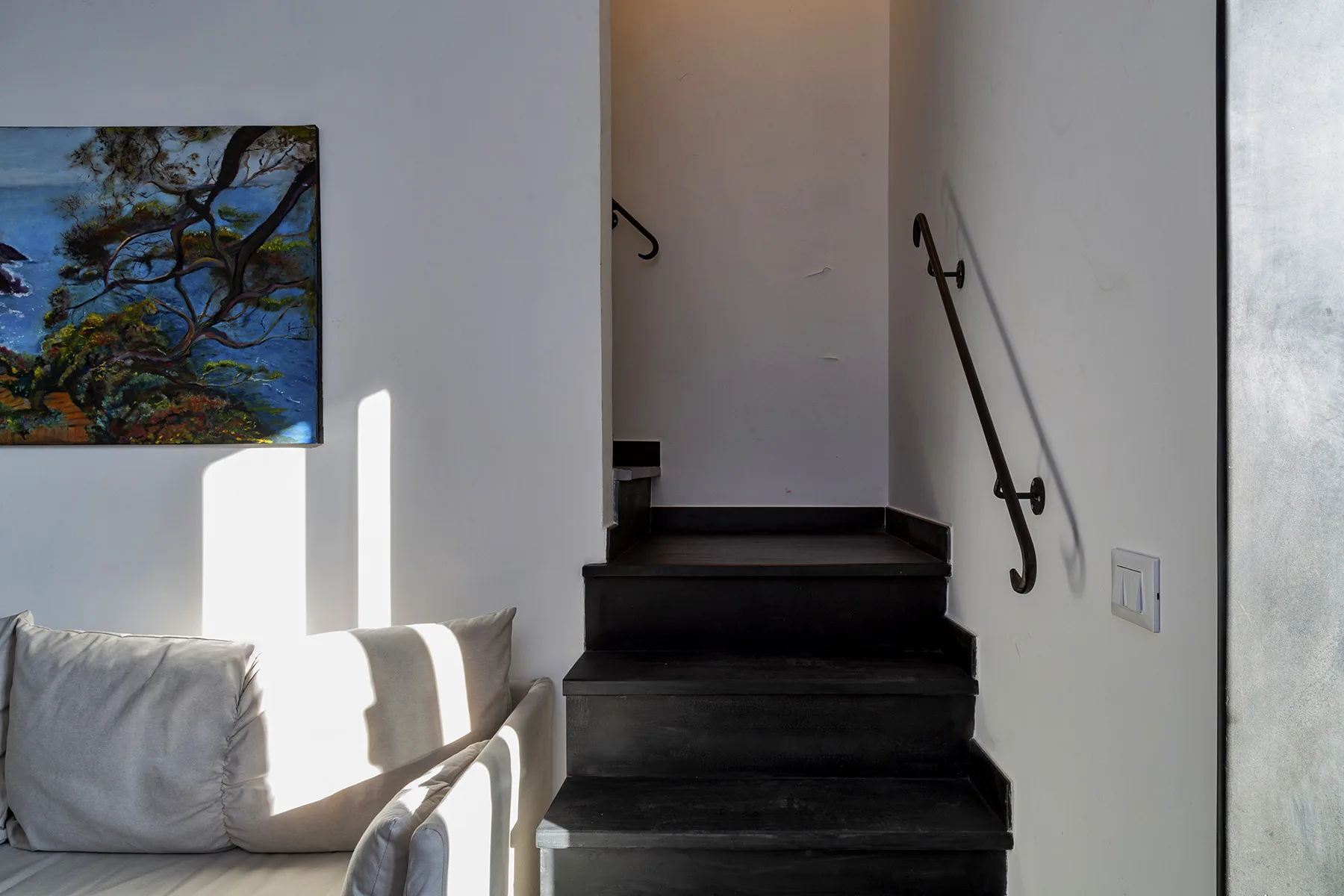 A dark staircase rises beside a seating area with a framed landscape painting.