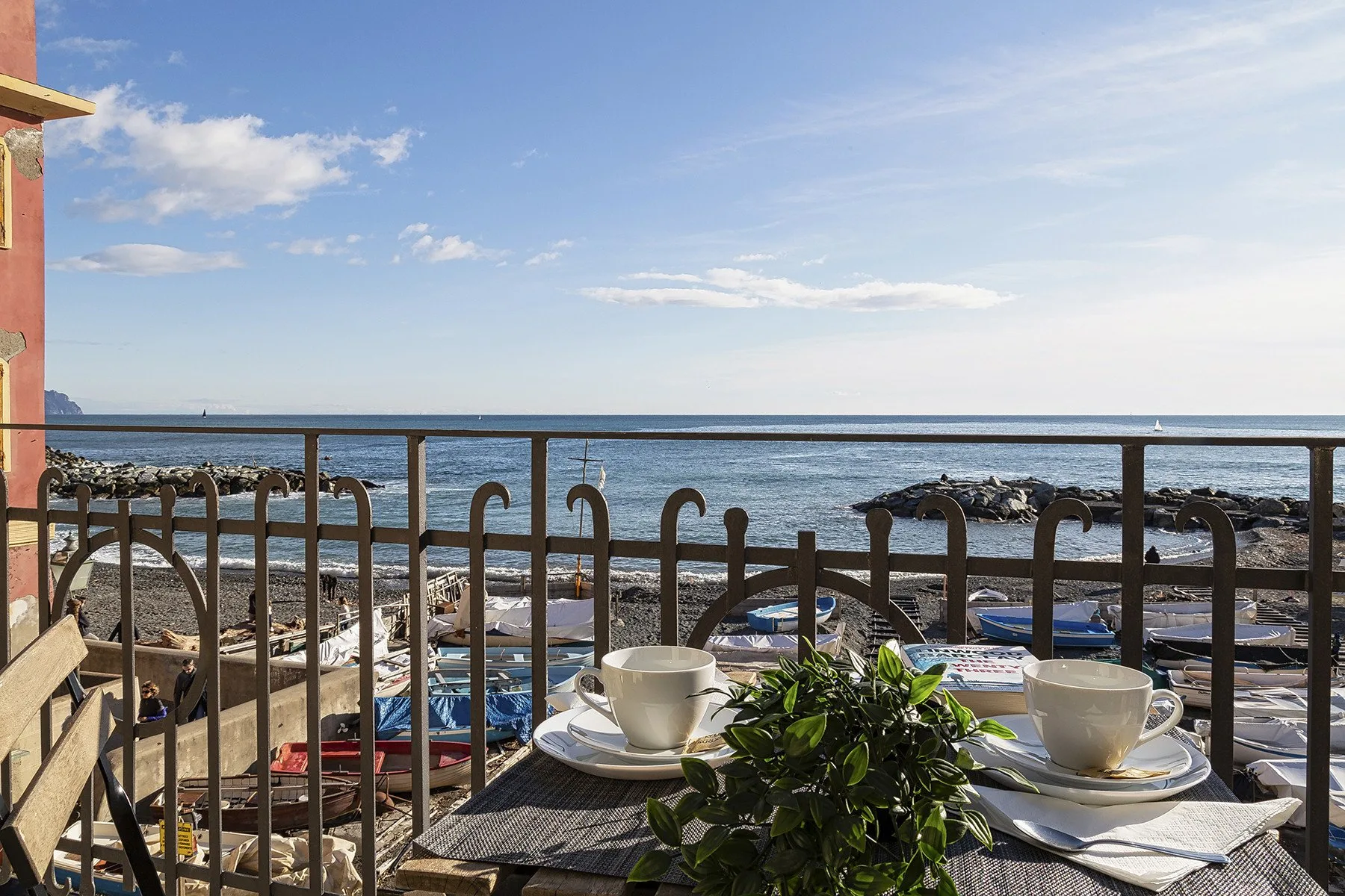 Una mesa junto al mar tiene tazas y plantas junto a una barandilla con vistas al agua.