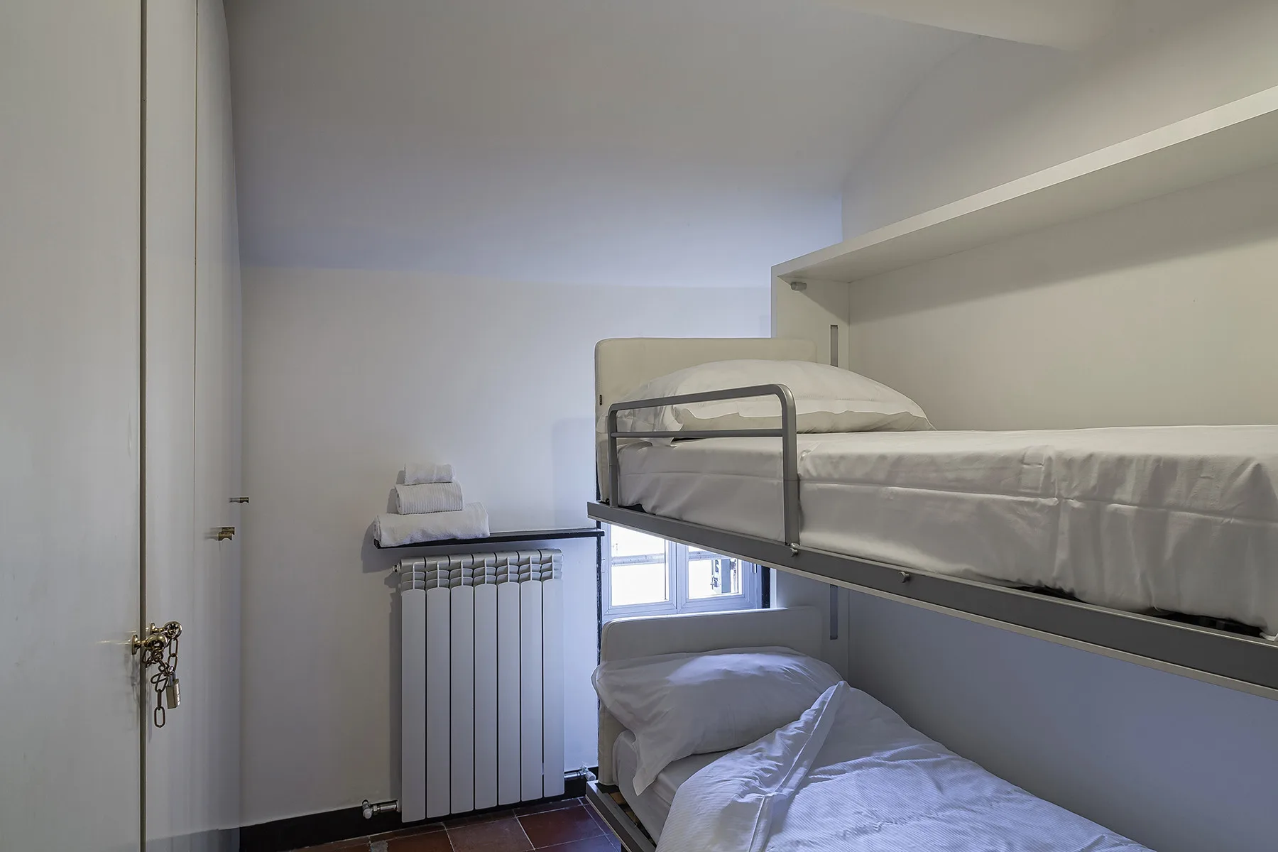 A compact bedroom with bunk beds and a radiator beneath the window.