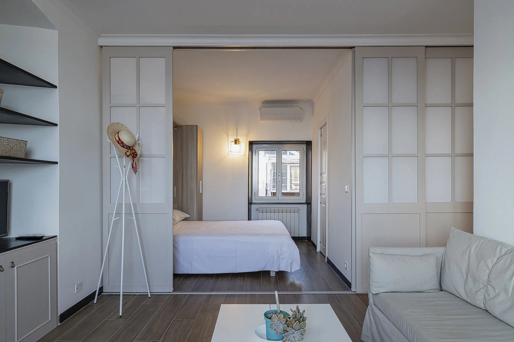 A bedroom with a bed, framed by sliding panels, and a seating area in the foreground.