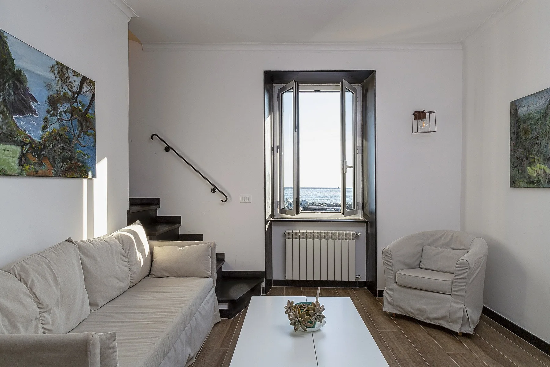 Una sala luminosa con asientos alrededor de una mesa blanca baja y una ventana abierta.