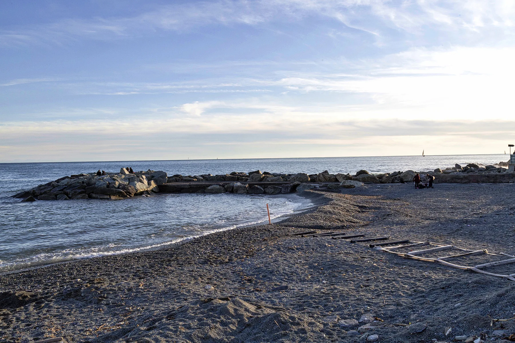 A rocky shoreline borders a dark sandy beach under a cloudy sky.