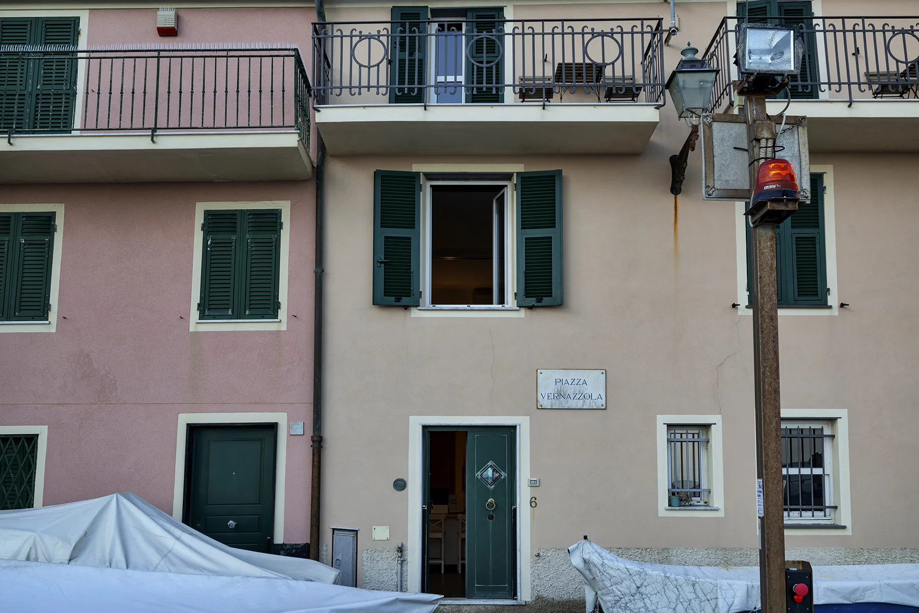 A pastel-colored building facade has shuttered windows, balconies, and a street-level entrance.