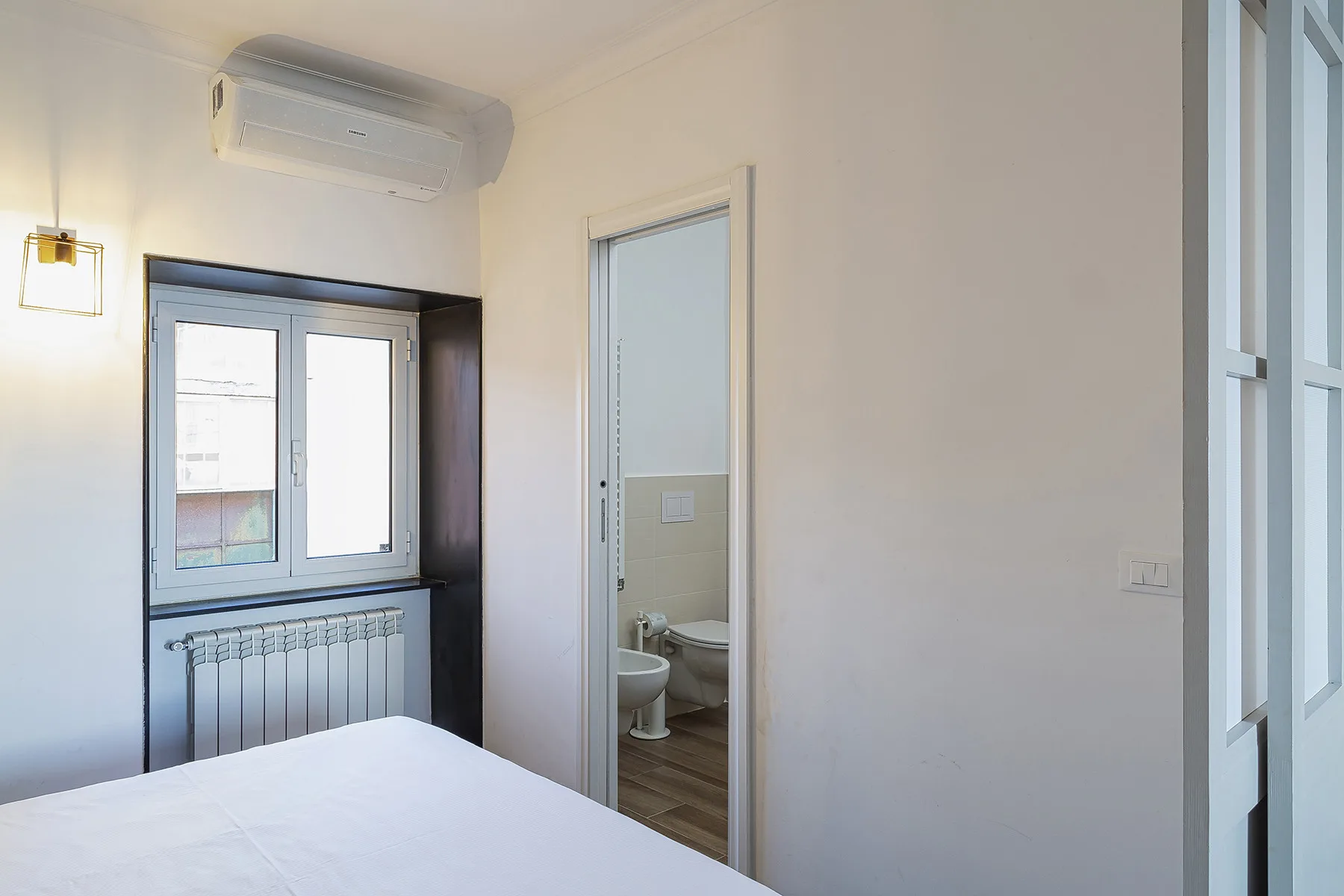 A bedroom with a bed beside a window and an open bathroom doorway.