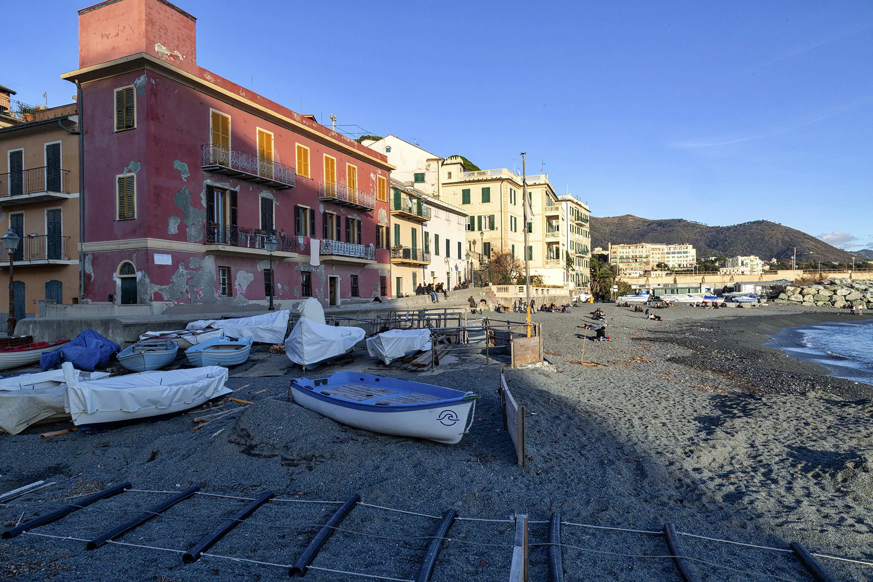 A coastal waterfront with colorful buildings, small boats, and a pebbled shore.