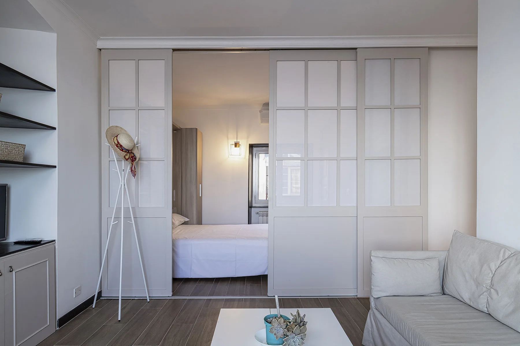 A bright bedroom opens into a sitting area with a bed and sofa.