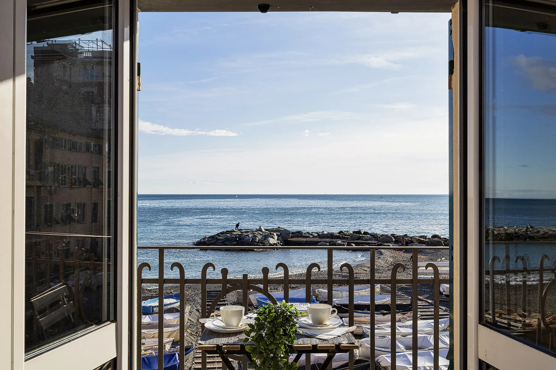 A balcony dining area overlooks the sea through an open glass doorway.
