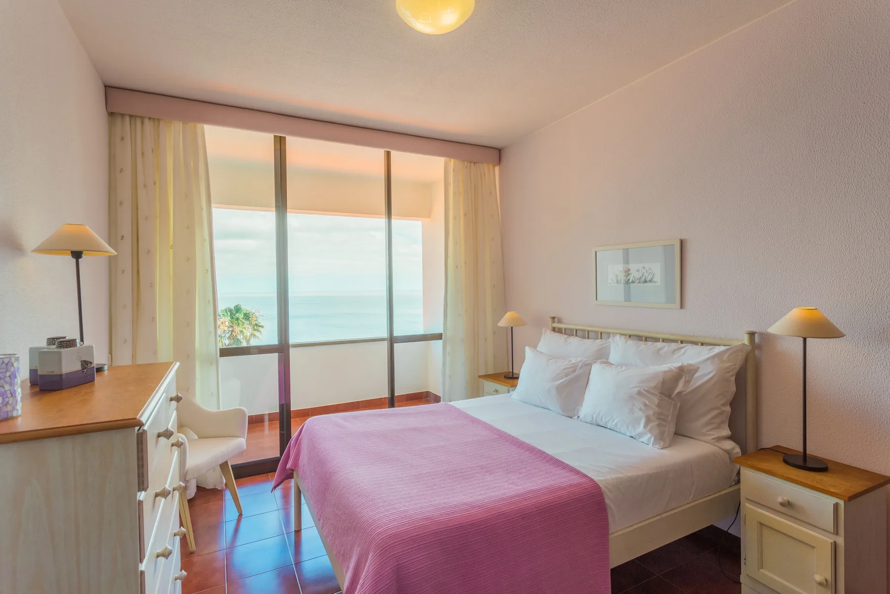 Un dormitorio con una cama cubierta de rosa y puertas correderas de cristal con vistas al mar.