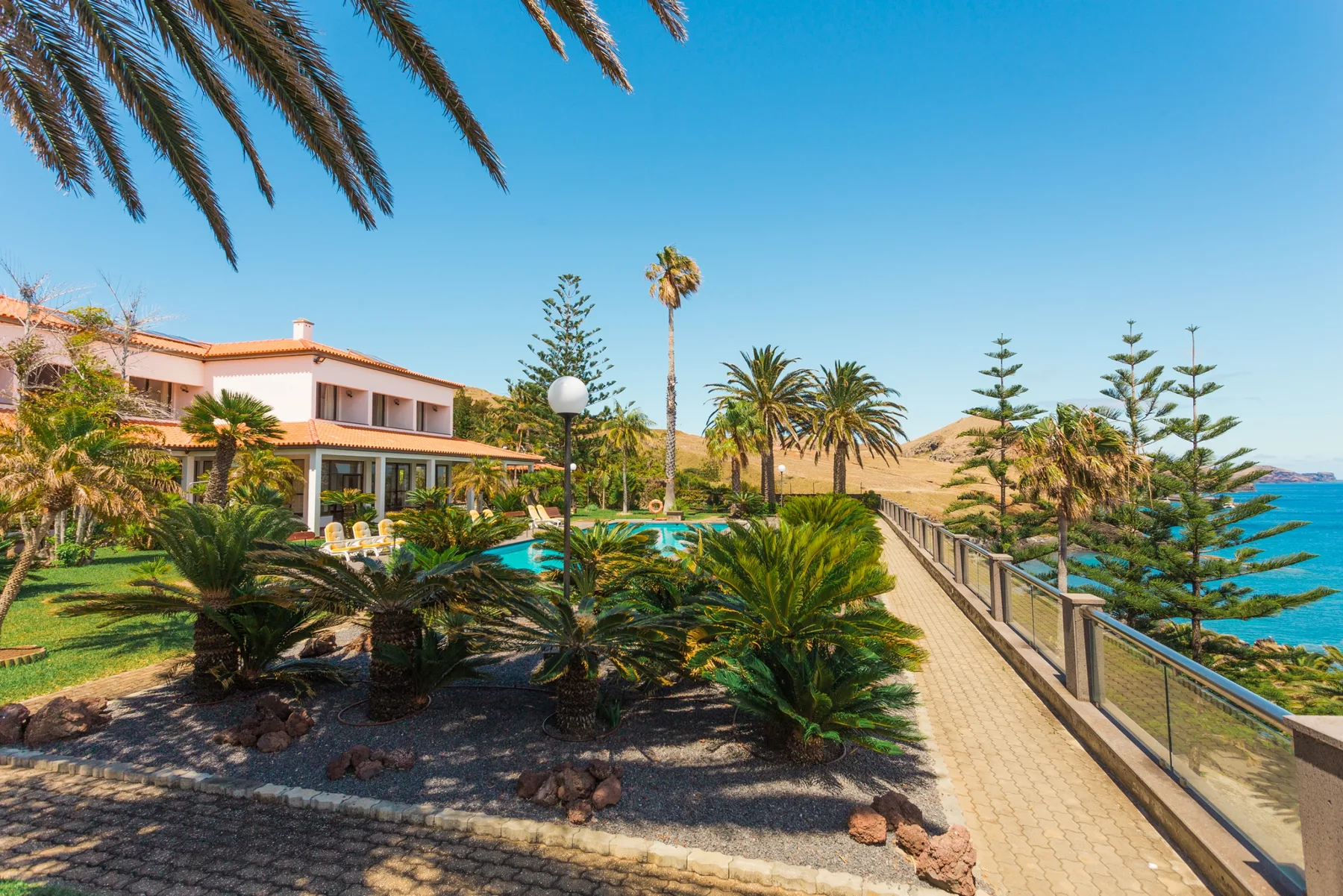 A landscaped coastal garden borders a paved walkway overlooking the ocean.