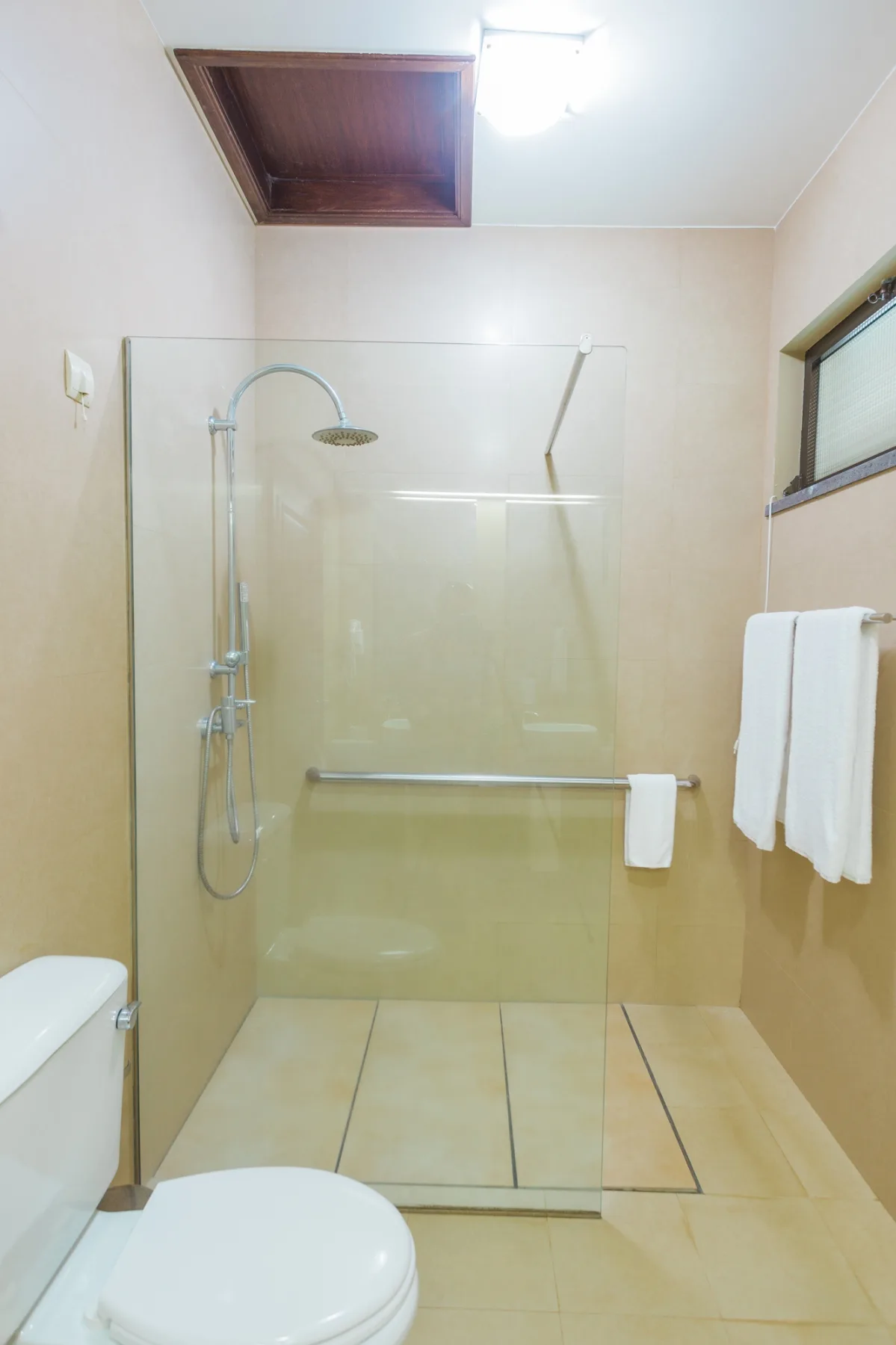 Un baño con una ducha de vidrio, un inodoro y toallas colgadas junto a la ventana.