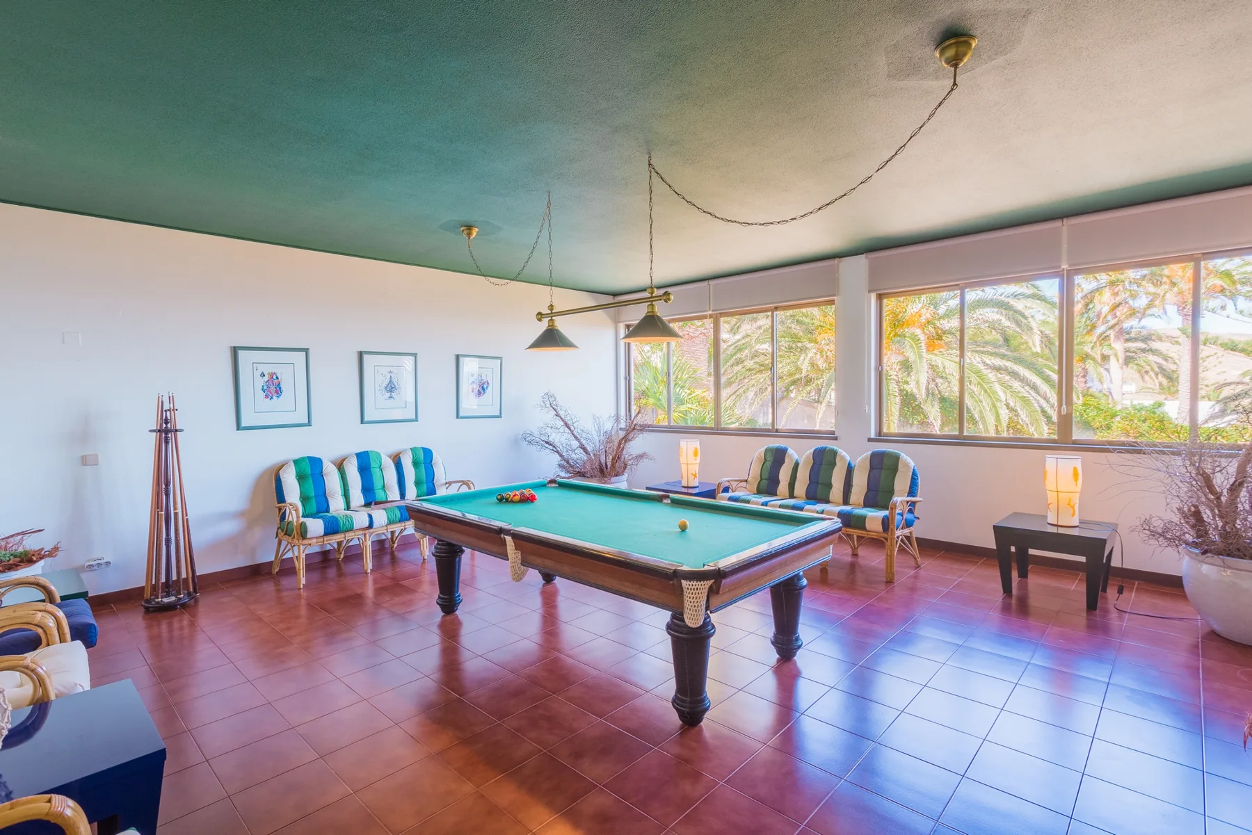 Una sala de billar con una mesa de billar y asientos junto a grandes ventanales.