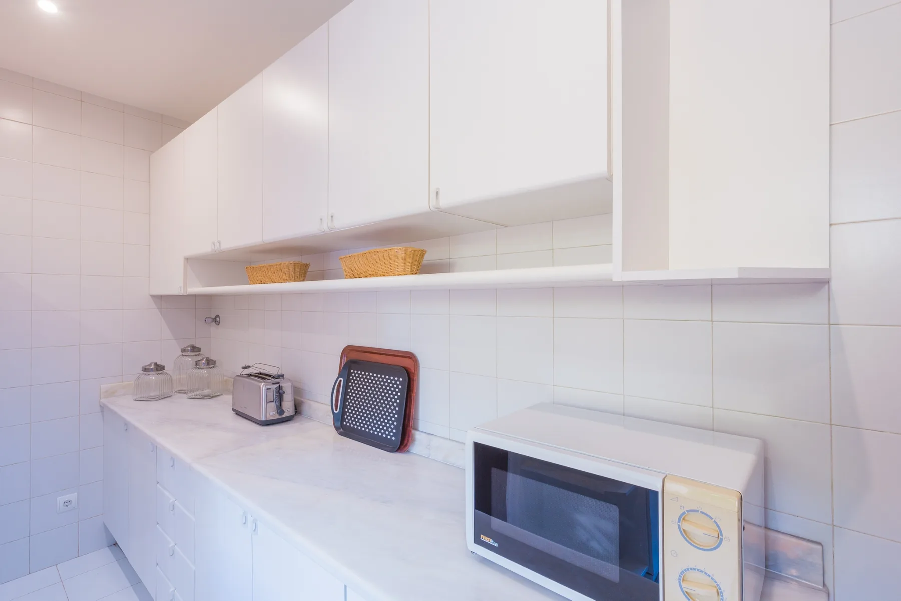 Una encimera de cocina luminosa con armarios blancos y pequeños electrodomésticos.