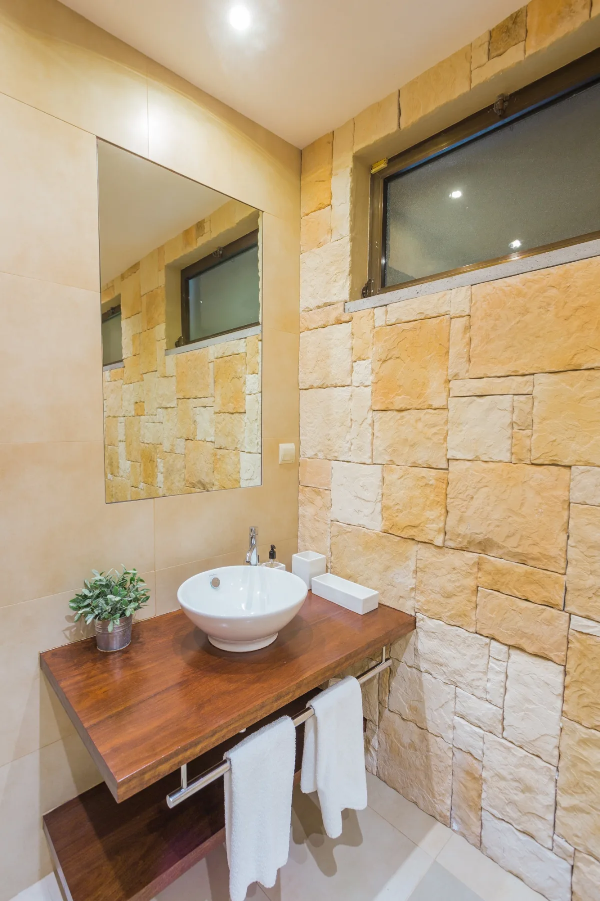 Un lavabo de baño con una palangana blanca, espejo y pared de piedra.