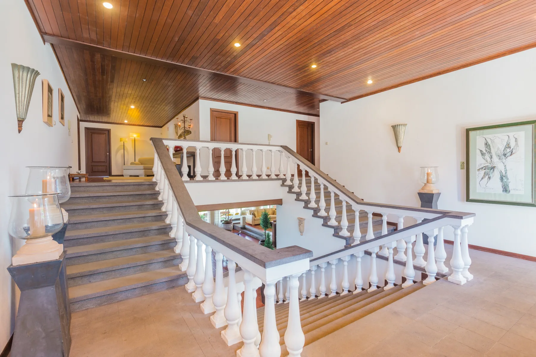 Descansillo interior con una escalera y balaustradas blancas bajo un techo de madera.