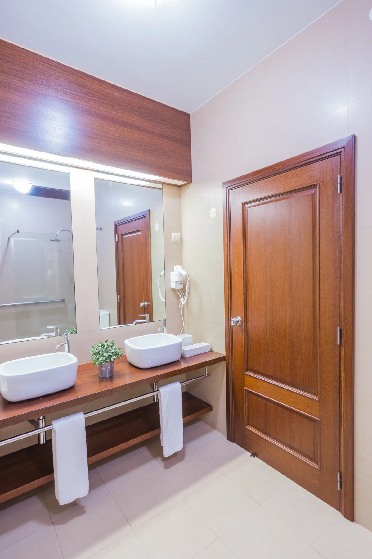Un lavabo de baño con dos lavamanos, espejos y una puerta de madera.
