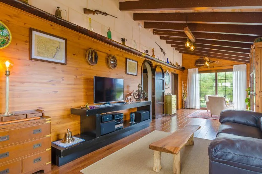 Una sala de estar revestida de madera, con televisión y asientos junto a grandes ventanas.
