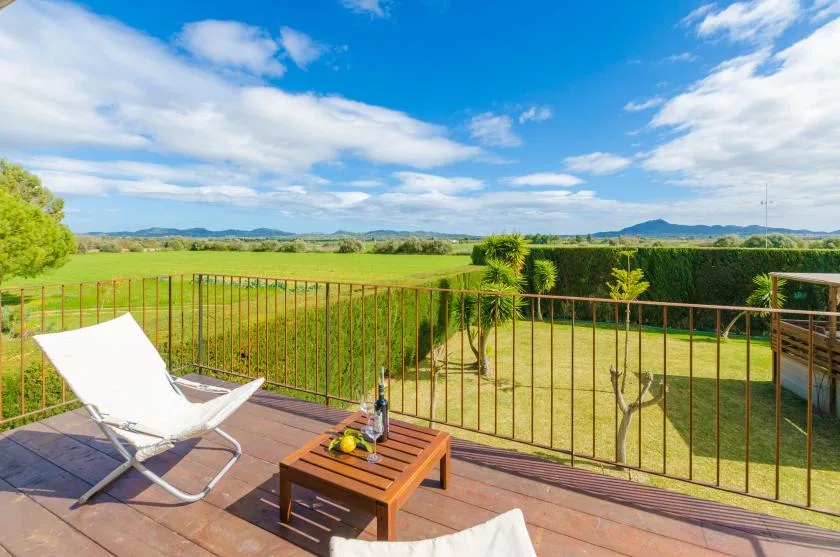 Una terraza soleada al aire libre da a un campo verde y colinas lejanas.