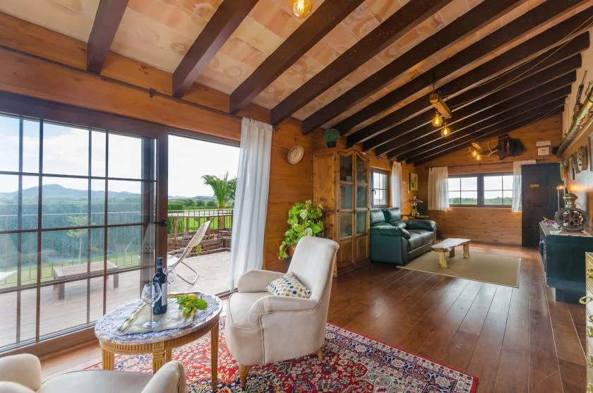 Una sala con vigas de madera se abre a una terraza mediante grandes puertas de vidrio.
