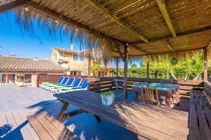 Una zona de comedor exterior a la sombra de una pérgola de madera da a una piscina.