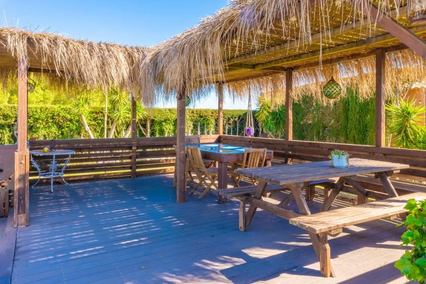 Una zona de comedor al aire libre con mesas de madera bajo un techo de paja.