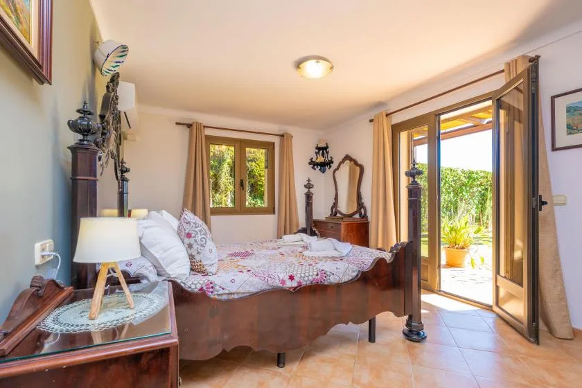 Un dormitorio con una cama de madera, ropa de cama floral y puertas abiertas al jardín.