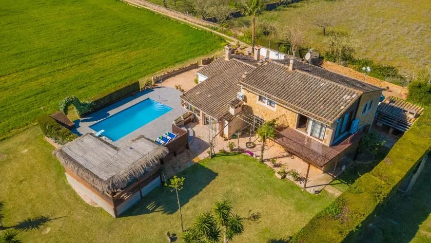 Vista aérea de una casa y una piscina junto a campos verdes abiertos.