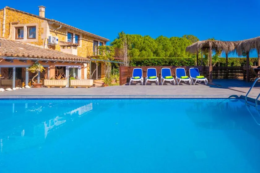 A swimming pool beside a stone house, with lounge seating along the deck.