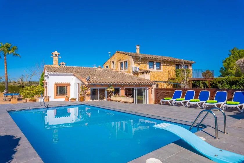Una piscina y tumbonas están frente a una casa grande.