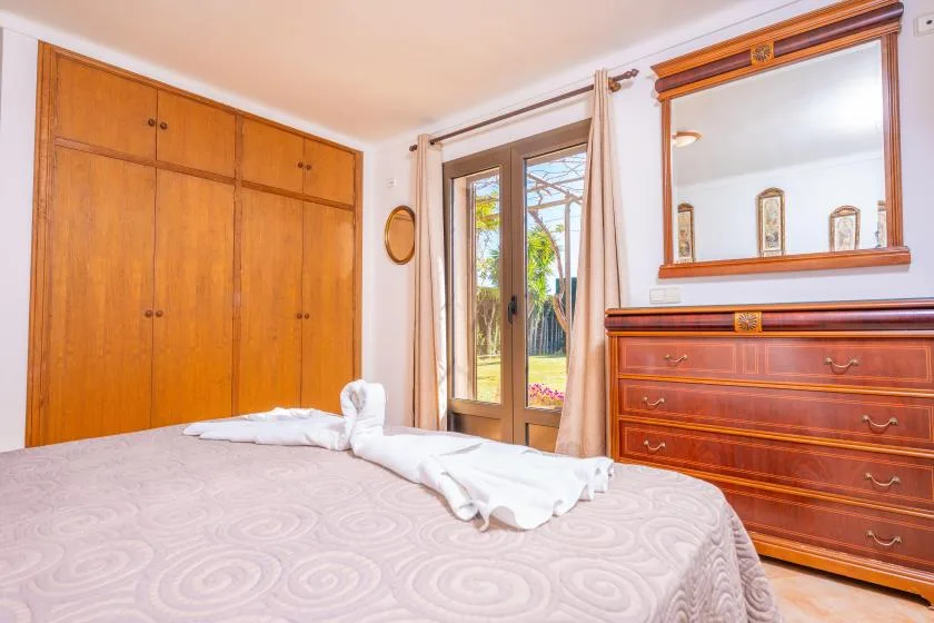 Un dormitorio con una cama, armarios de madera y puertas de cristal que dan a un jardín.