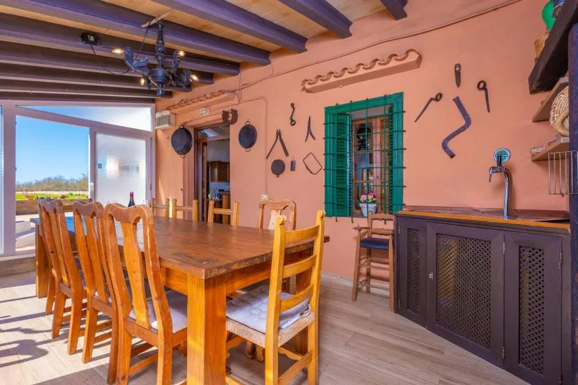 Un comedor con una mesa larga de madera, sillas y herramientas decorativas en la pared.