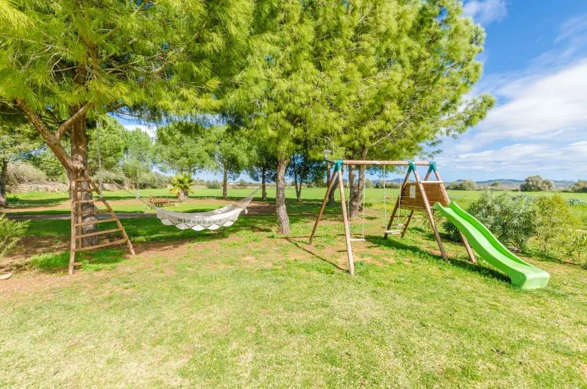 Zona de juegos al aire libre con columpios y una hamaca bajo los árboles.