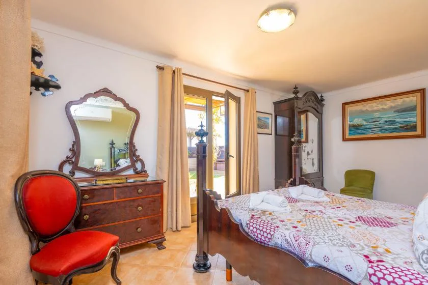 Un dormitorio con una colcha estampada, una cómoda de madera y una ventana abierta.