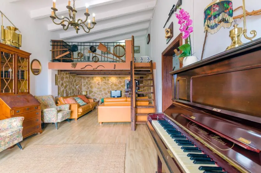 Una sala de estar con un piano vertical y una zona elevada para dormir.