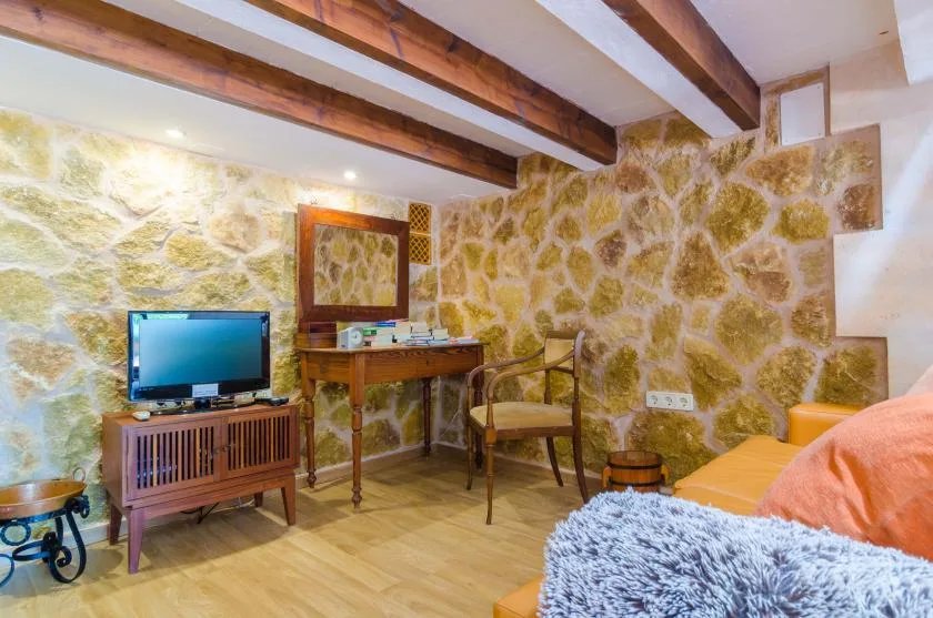 Una habitación con paredes de piedra, escritorio, televisor y asientos.