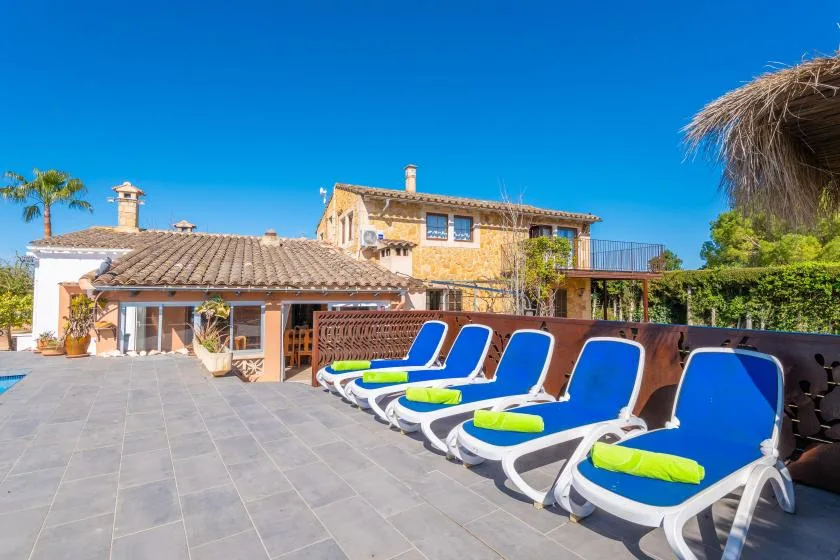 Un patio soleado con tumbonas azules junto a una casa con techo de tejas.