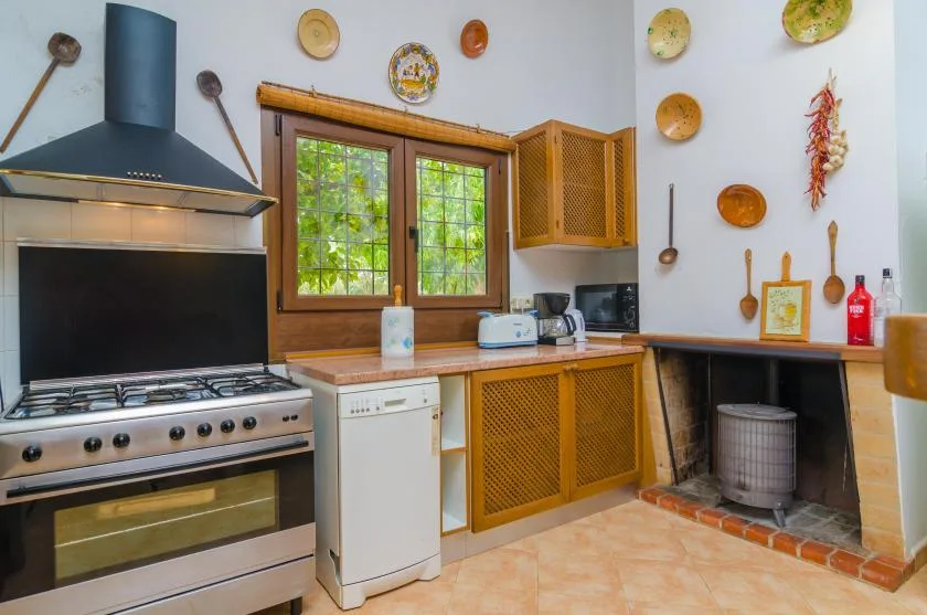 Una cocina rústica con estufa, fregadero y gabinetes de madera bajo una ventana.