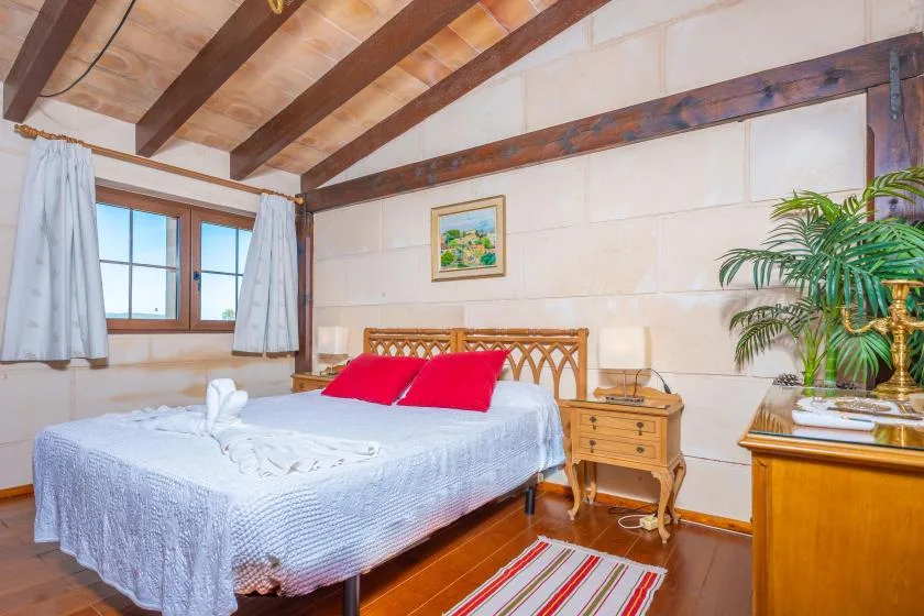 Un dormitorio con una cama, almohadas rojas y una ventana al lado.
