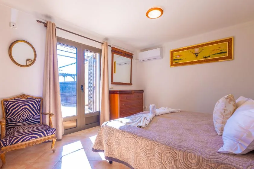 Un dormitorio con una cama, un sillón estampado y puertas de vidrio que dan a un balcón.