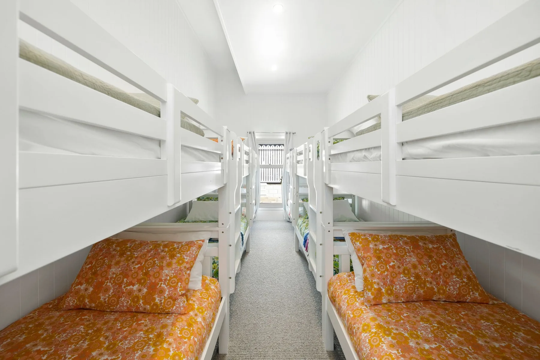 Un dormitorio luminoso con literas blancas y ropa de cama estampada en tonos naranjas.