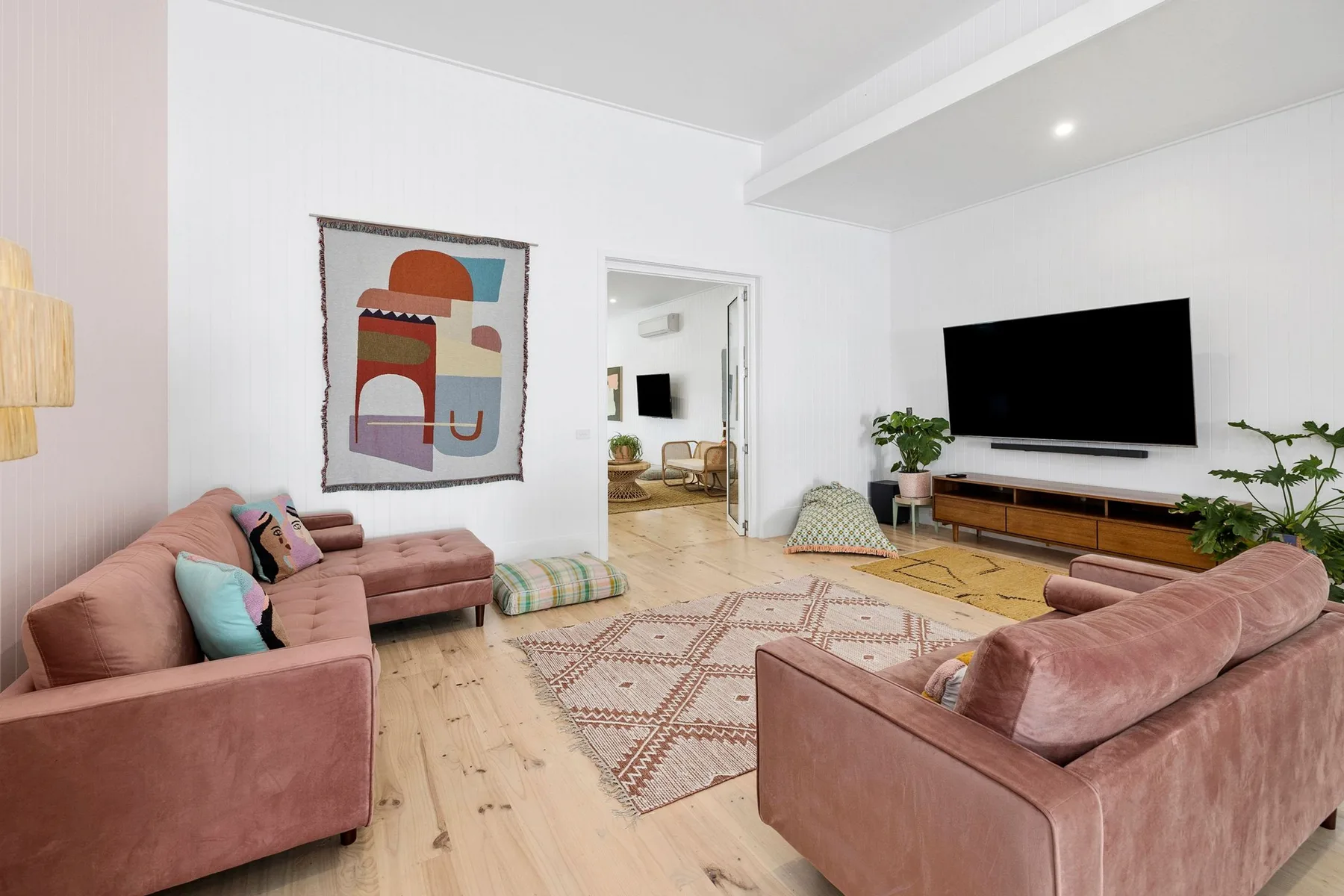 Una sala luminosa con asientos rosados, una alfombra estampada y un televisor en la pared.