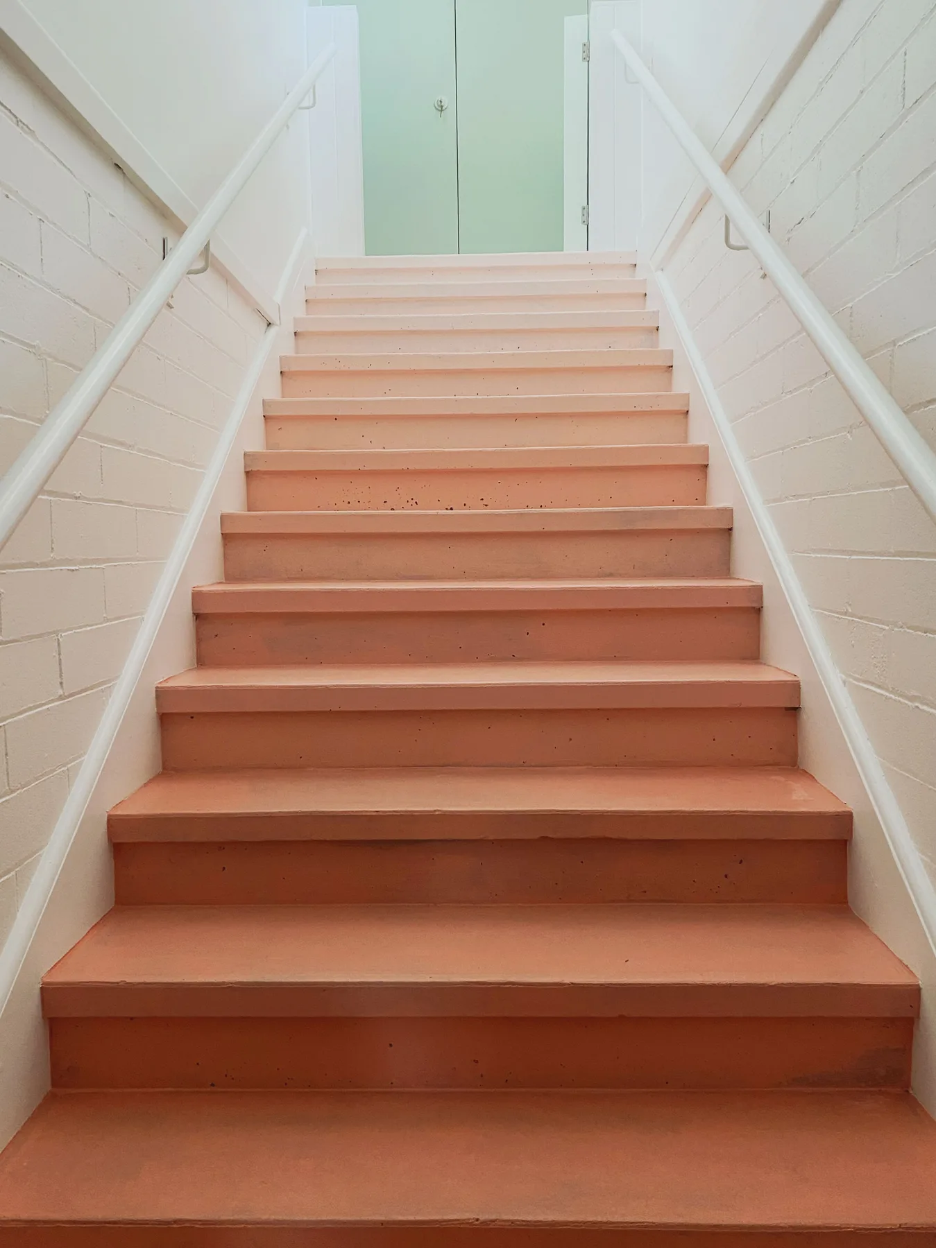 Una escalera con peldaños color terracota y pasamanos blancos.
