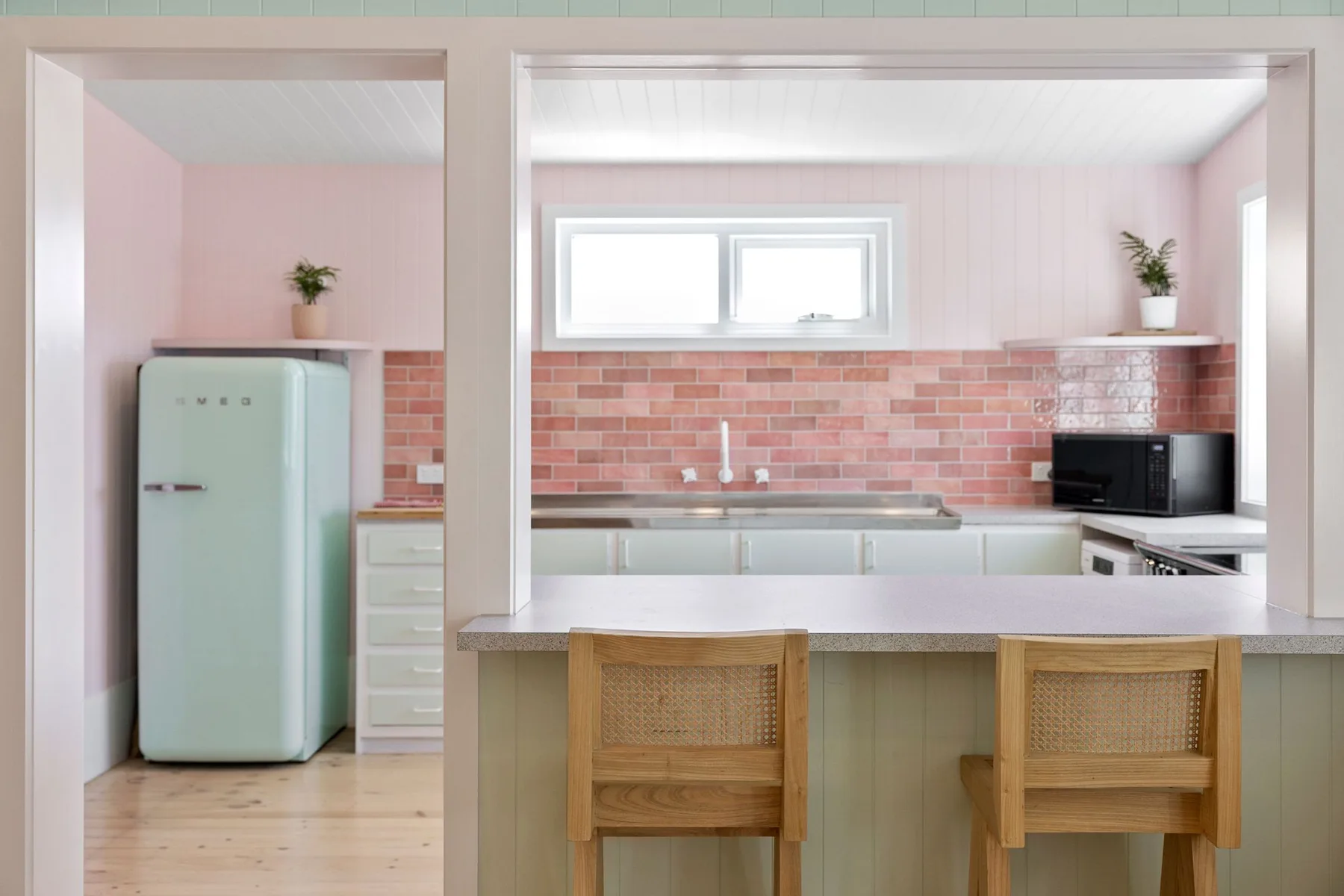 Una cocina rosa con una barra, taburetes de madera y un refrigerador verde claro.