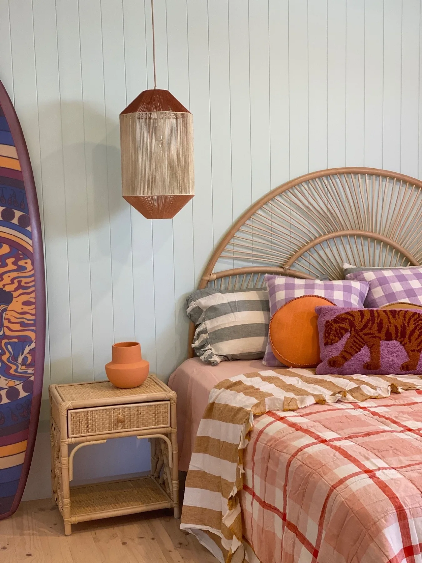Un dormitorio con cabecero de ratán, ropa de cama estampada y una mesita de noche.