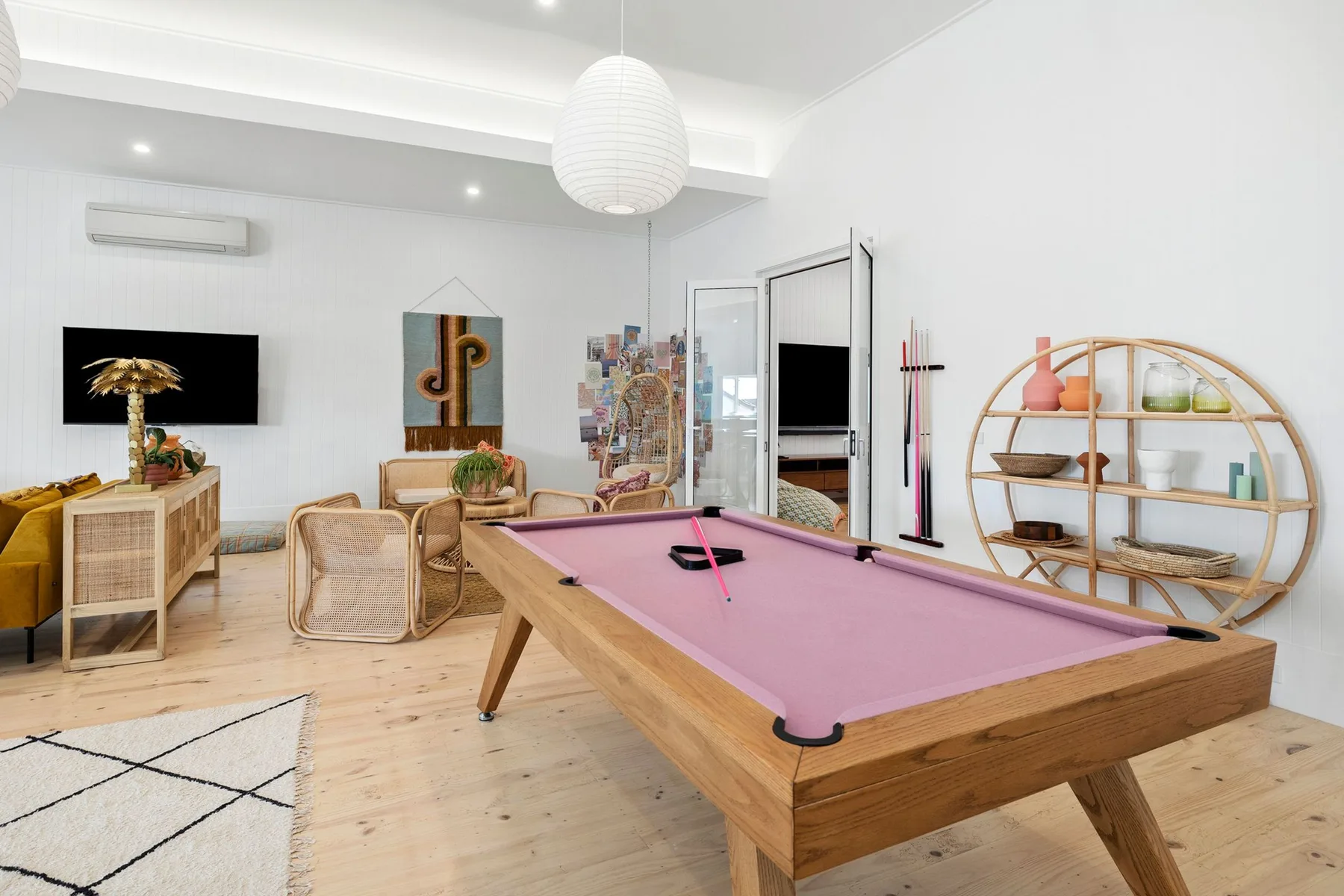 Una luminosa sala de juegos tiene una mesa de billar con paño rosa y asientos informales.