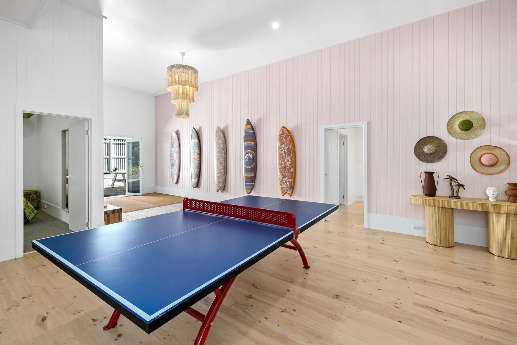 Una sala recreativa con una mesa de ping pong azul y tablas de surf en la pared.