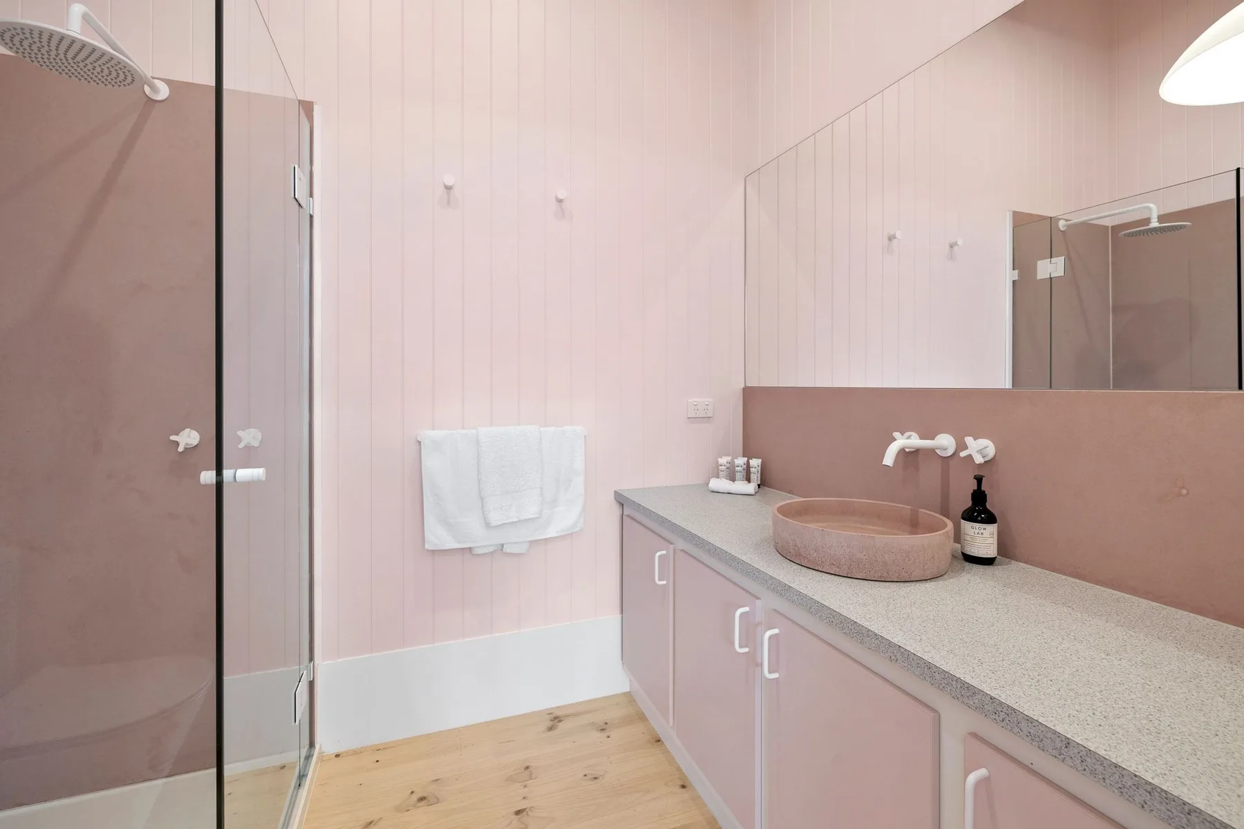 Baño rosa con una ducha de vidrio y un mueble de lavabo alargado.