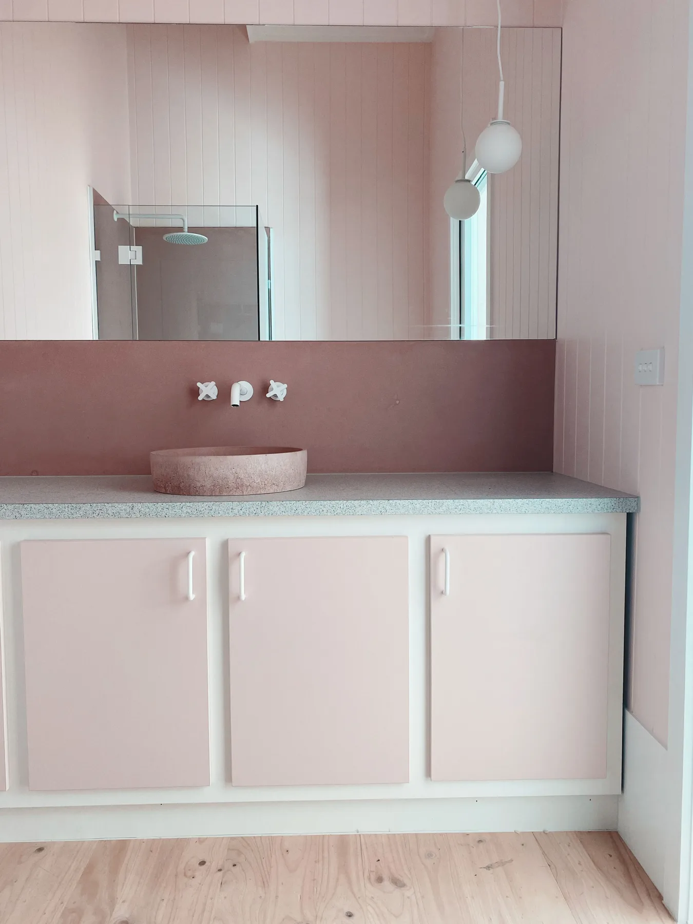 Un tocador de baño rosa con un lavabo redondo bajo un espejo grande.